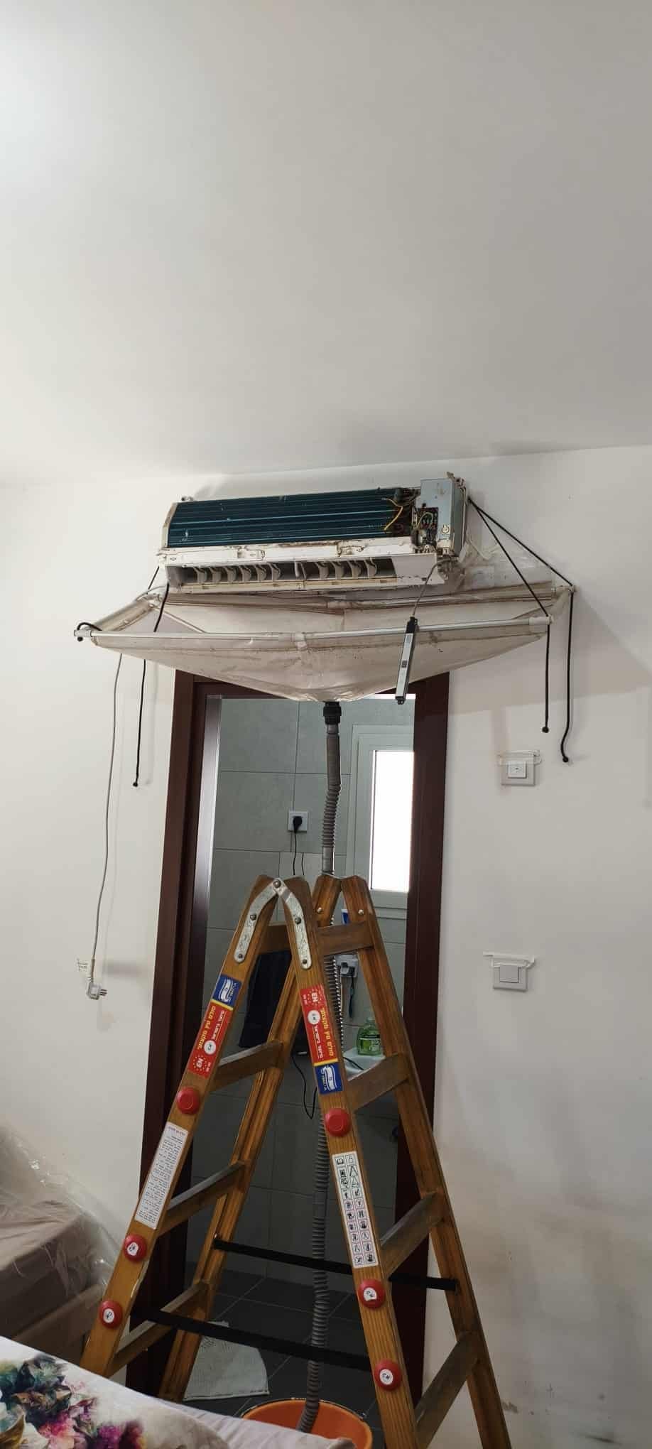 Mini split being cleaned using wash bag and ladder